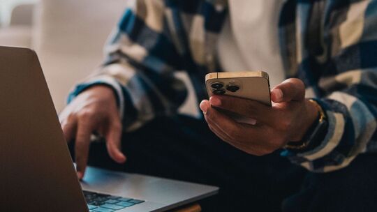 Ein Mann arbeitet am Laptop und hält ein Smartphone in der Hand