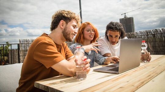 Junge Leute sitzen auf einer Dachterrasse vor einem Laptop