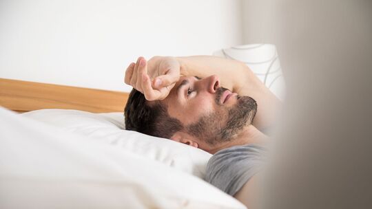 Mann liegt schlaflos im Bett