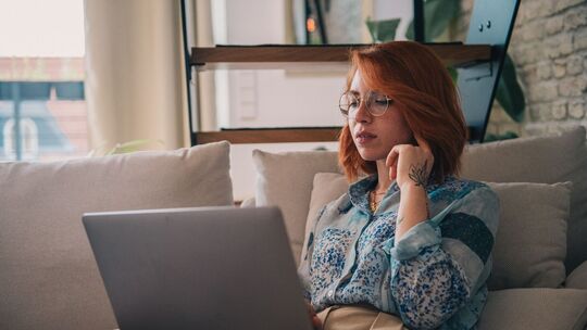 Eine Frau sitzt auf der Couch und nutzt einen Laptop