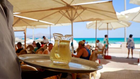 Ein Kellner serviert an einem mallorquinischen Strand einen Wein