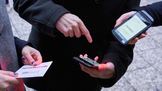 Ein Mann zeigt auf einen QR-Code den eine Frau Scannt