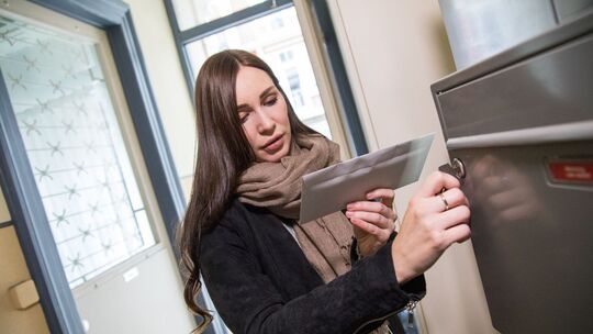 Eine Frau holt einen Brief aus dem Briefkasten Eine Frau holt einen Brief aus dem Briefkasten