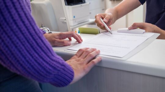 Arzthelfer übergibt Patientin einen Anamnesebogen
