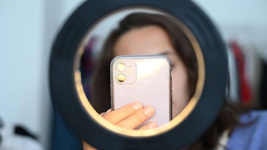 Frau sitzt hinter einem Ringlicht und macht dabei Aufnahmen