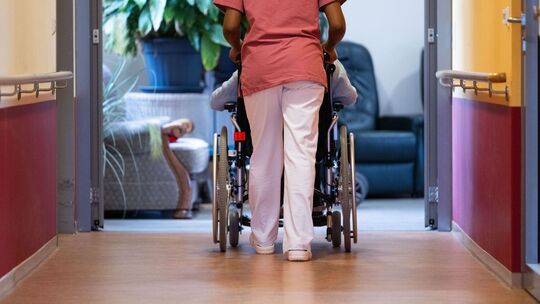 Eine Pflegekraft schiebt einen Pflegebedürftigen im Rollstuhl Eine Pflegekraft schiebt einen Pflegebedürftigen im Rollstuhl