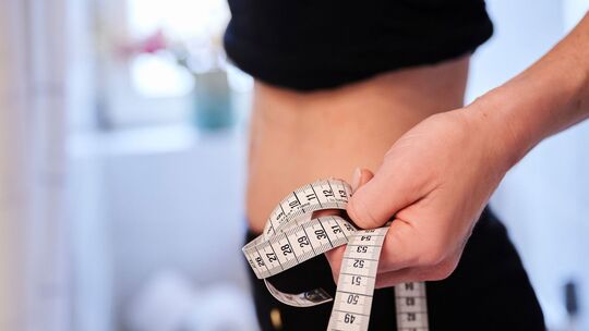 Eine junge Frau hält ein Zentimetermaßband an ihren Bauch