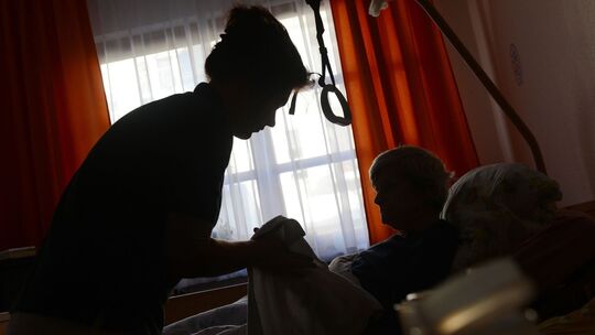 Frau wird in ihrem Bett von einer Pflegerin betreut