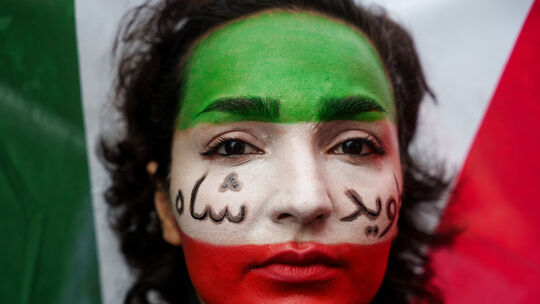 Eine Frau zeigt die Farben der iranischen Flagge im Gesicht - Grün, Weiß und Rot - sowie einen aufgemalten Schriftzug auf Persis