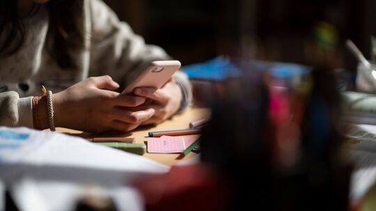 Eine Jugendliche sitzt mit Smartphone an einem Schreibtisch