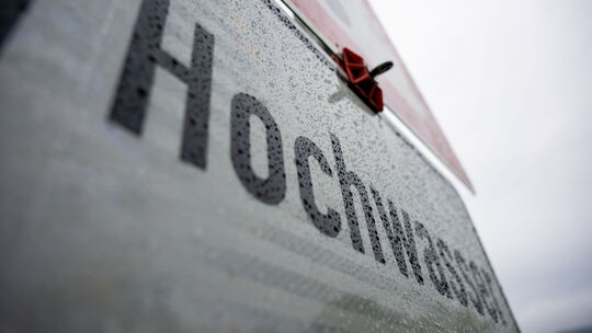 Regentropfen hängen an einem Schild, das vor Hochwasser warnt, Wolken am Himmel verheißen weiteren Niederschlag. Zum Ende der Pf
