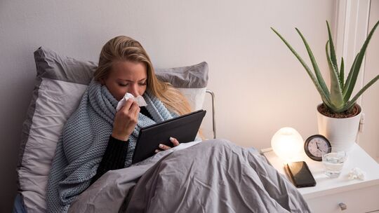 Eine Frau liegt krank im Bett und guckt auf ihren Tablet-Computer Eine Frau liegt krank im Bett und guckt auf ihren Tablet-Computer