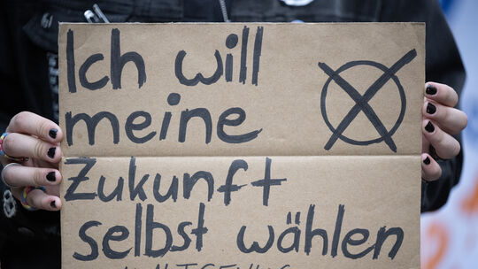 Eine Teilnehmerin hält während einer Demonstration auf dem Ernst-Ludwig-Platz in Mainz ein Schild in die Kamera. Denn der rheinl