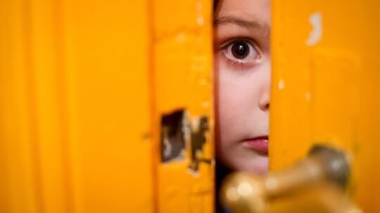 Kind schaut durch einen Türschlitz