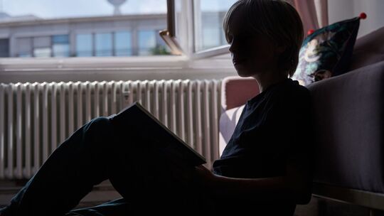 Ein Kind liest an eine Couch gelehnt