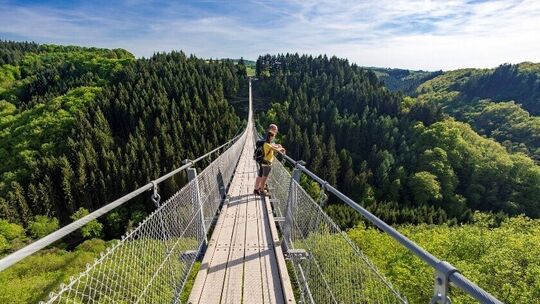 Wanderer überquert die Hängeseilbrücke Geierlay mit Blick über bewaldete Hügel.