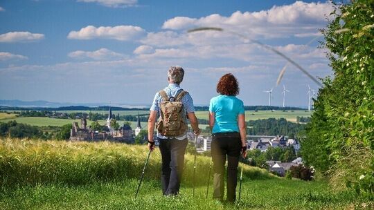 Zwei Wanderer gehen auf einem Wiesenweg mit Blick auf Kastellaun und Windräder.