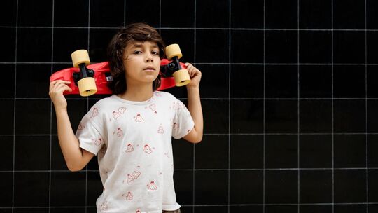 Selbstbewußter Junge trägt ein Skateboard auf seinen Schultern