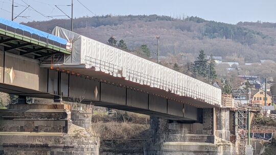 Von der Seite aus sieht man das Zelt gut, in das das Arbeitsgerüst eingehaust ist. So können die Beschichtungen der alten Träger Wie der Fuß- und Radweg über den Rhein verbreitert wird.