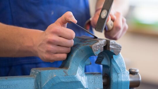 Auszubildender steht mit einem Hammer an einem Schraubstock