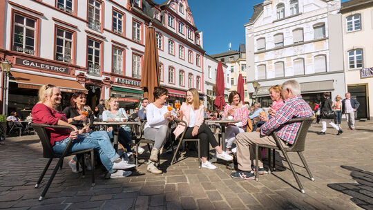 Touristen in der Stadt genießen das sonnige Wetter auf dem Jesuitenplatz in Koblenz. Voraussichtlich ab Herbst 2026 sollen Übern