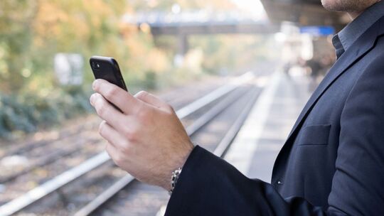Mann mit Smartphone am Gleis