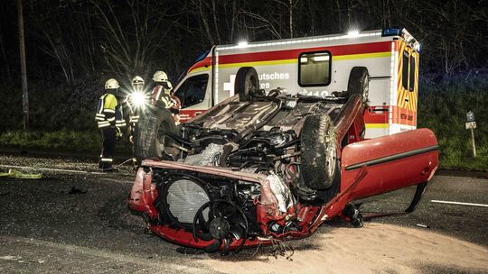 Das völlig zerstörte Fahrzeug liegt auf dem Dach, während Einsatzkräfte die Unfallstelle sichern. Trotz des heftigen Unfalls auf