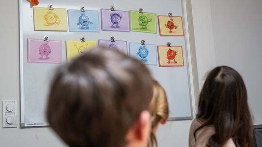 Grundschüler schauen auf eine Wand mit Grafiken, mit denen sie ihre eigene Gefühlslage beschreiben können. "Für Kinder ganz wich