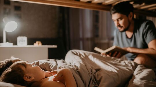 Vater liest seinen Kindern bei der Einschlafbegleitung etwas vor