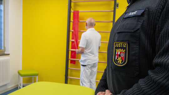 Ein Justizbeamter der Justizvollzugsanstalt (JVA) Wittlich steht im Raum für Physiotherapie, während ein Therapeut Vorbereitunge