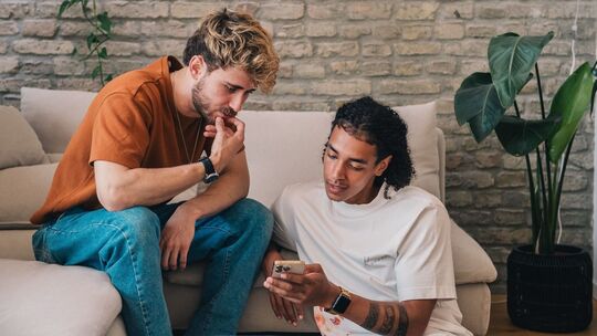 Zwei junge Männer mit Smartphone auf einer Couch