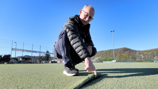 Ortsbürgermeister Oliver Labonde zeigt die kaputten Stellen auf dem Kunstrasenplatz, der in die Jahre gekommen ist.