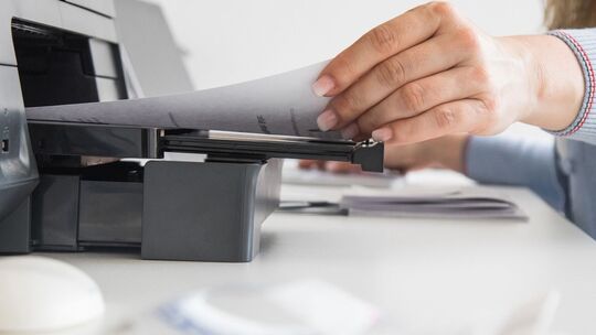 Frau nimmt ein Blatt Papier aus einem Drucker
