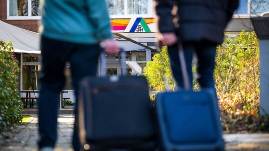 Gäste stehen mit Koffern und Taschen vor einer Jugendherberge
