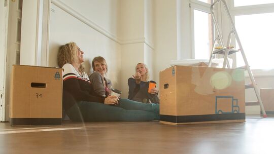 Drei Frauen sitzen gut gelaunt zwischen Umzugskisten