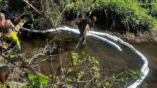 Hilfskräfte versuchen, die Ausbreitung des Dieselkraftstoffs im Bach mit Ölschläuchen zu verhindern.