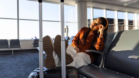 Eine Frau mit Kopfhörern wartet am Gate auf einen Flug