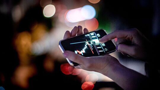 Mann hält ein Smartphone mit einer Trading-App in der Hand Mann hält ein Smartphone mit einer Trading-App in der Hand