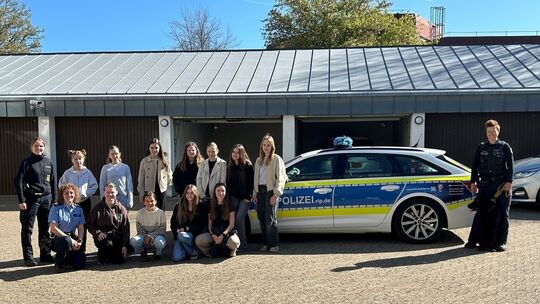 Zwei Polizistinnen, elf Mädchen und eine Diensthundeführerin mit Diensthund vor einem Streifenwagen