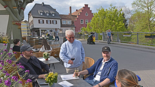 Gastgeber Werner Klopfer (stehend) freut sich, wenn Weinfreunde seine Tische und Stühle vor dem Brückenhaus nutzen, um regionale