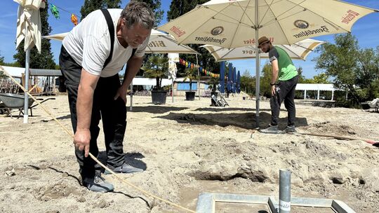 Klaus Berg (vorn) und sein Helfer Finn bauen die Schirmständer auf. Dazu messen sie auf dem verteilten Sand des Stattstrands die
