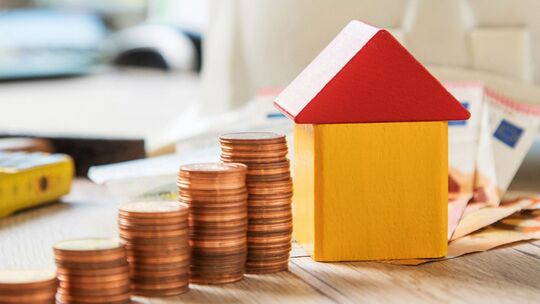 Münzen und ein Haus aus Bausteinen liegen auf einem Tisch