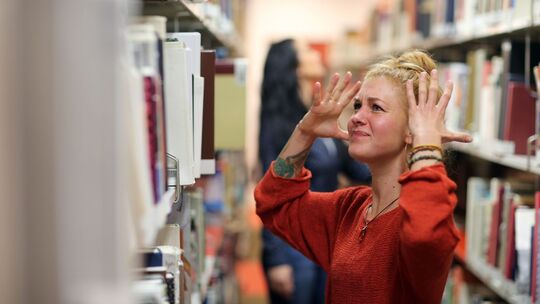 Frau steht wütend vor einem Bücherregal in der Unibibliothek