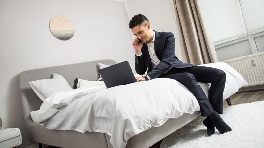 Ein Mann im Anzug sitzt auf einem Bett vor seinem Laptop