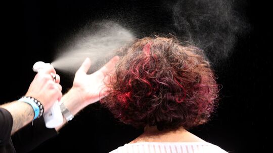 Ein Friseur sprüht einer Frau die Haare mit Haarspray ein