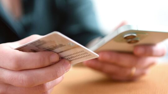 Eine Frau hält Personalausweis und Smartphone in den Händen