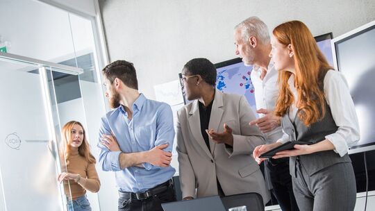 Eine Kollegin hebt die Uhr in einem Meeting mit anderen Kollegen