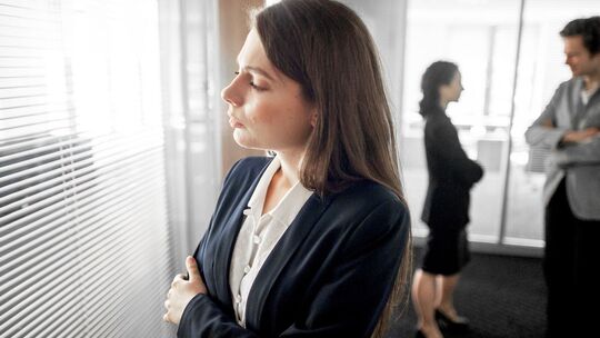 Frau steht abseits ihrer Kollegen in einem Büro