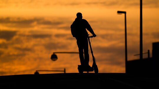 Mann fährt mit einem E-Scooter über eine Brücke