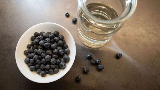 Blaubeeren liegen in einer Schale neben einem Glas Wasser